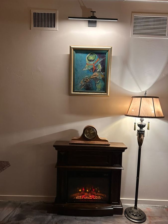 Coin salon du bistro, tableau d'un joueur de flûte, horloge ancienne et foyer allumé sous une lampe sur pied