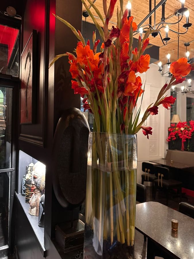 Glaïeuls orange dans un vase de verre devant des sculptures, lustres à chandelles au plafond de bois