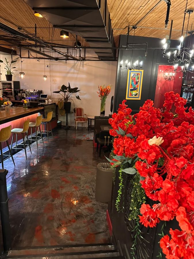 Le bar du bistro, tabourets ocre, fleurs rouges et sol de béton ciré aux éclats rouges